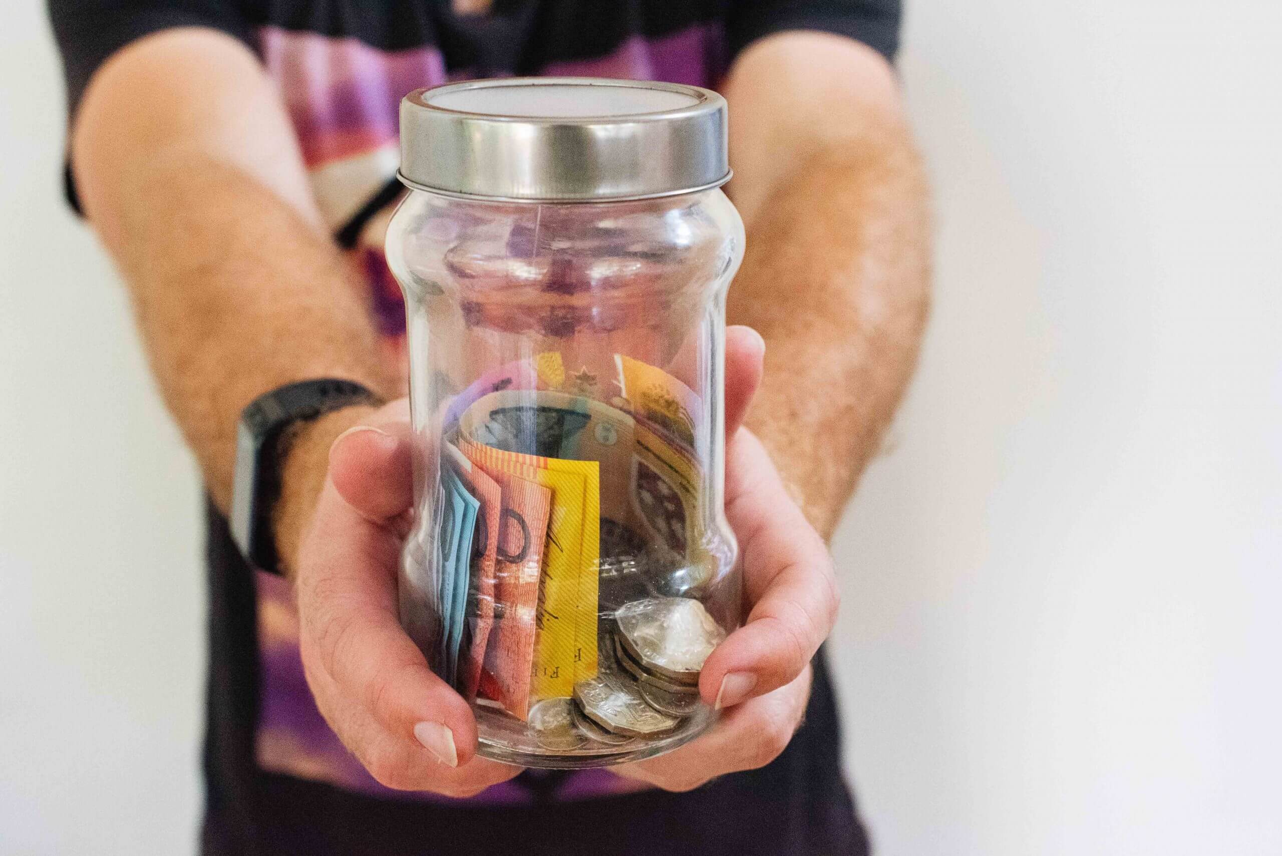 A man holding out a jar with some cash and coins