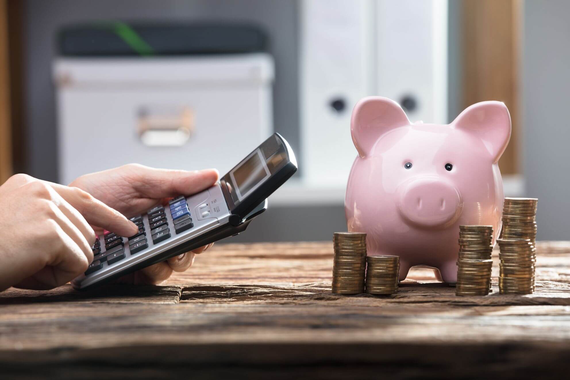 A piggy bank next to some coins and a person holding a calculator