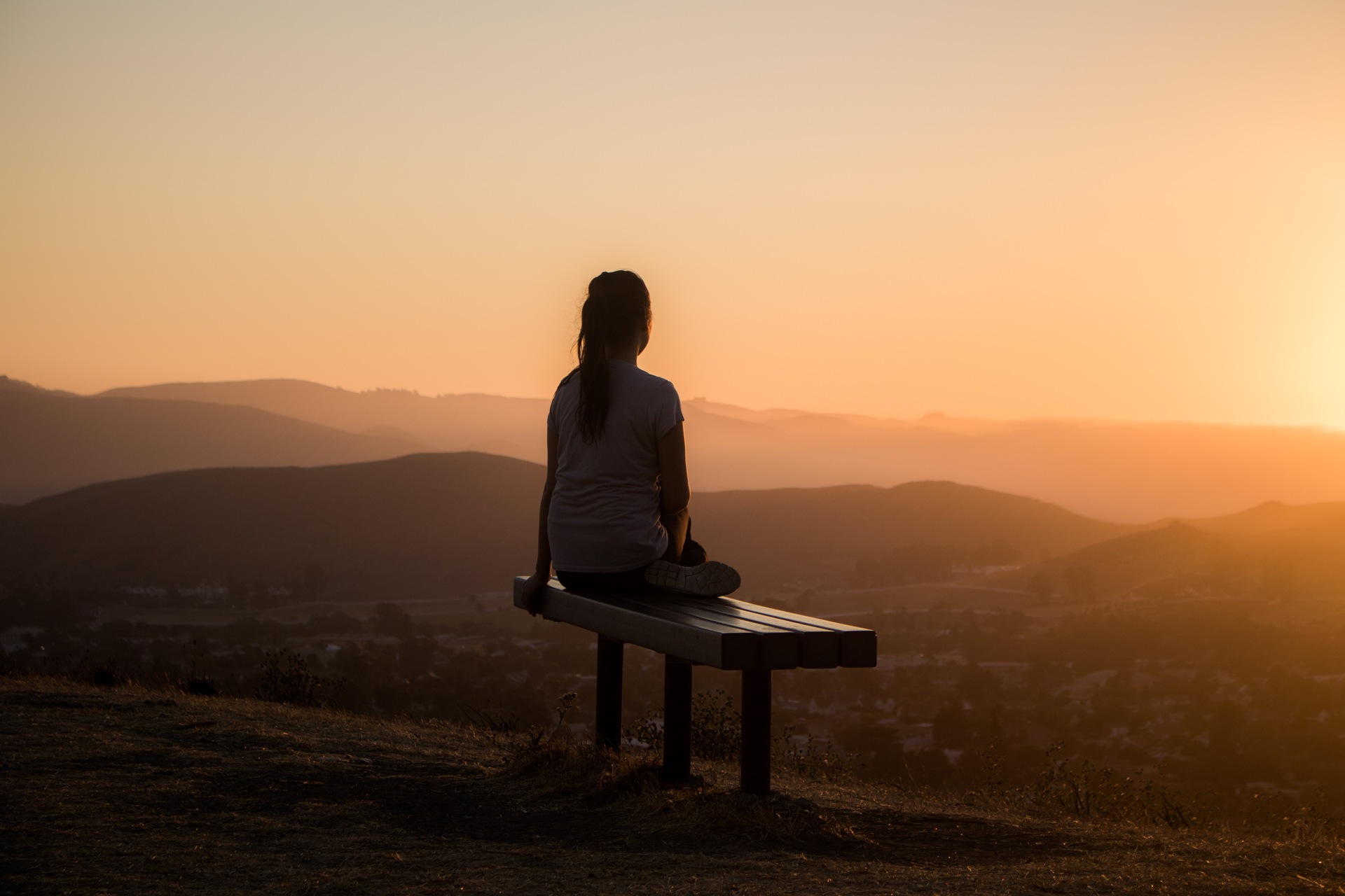 Girl looking at a sunset while sitting on a bench