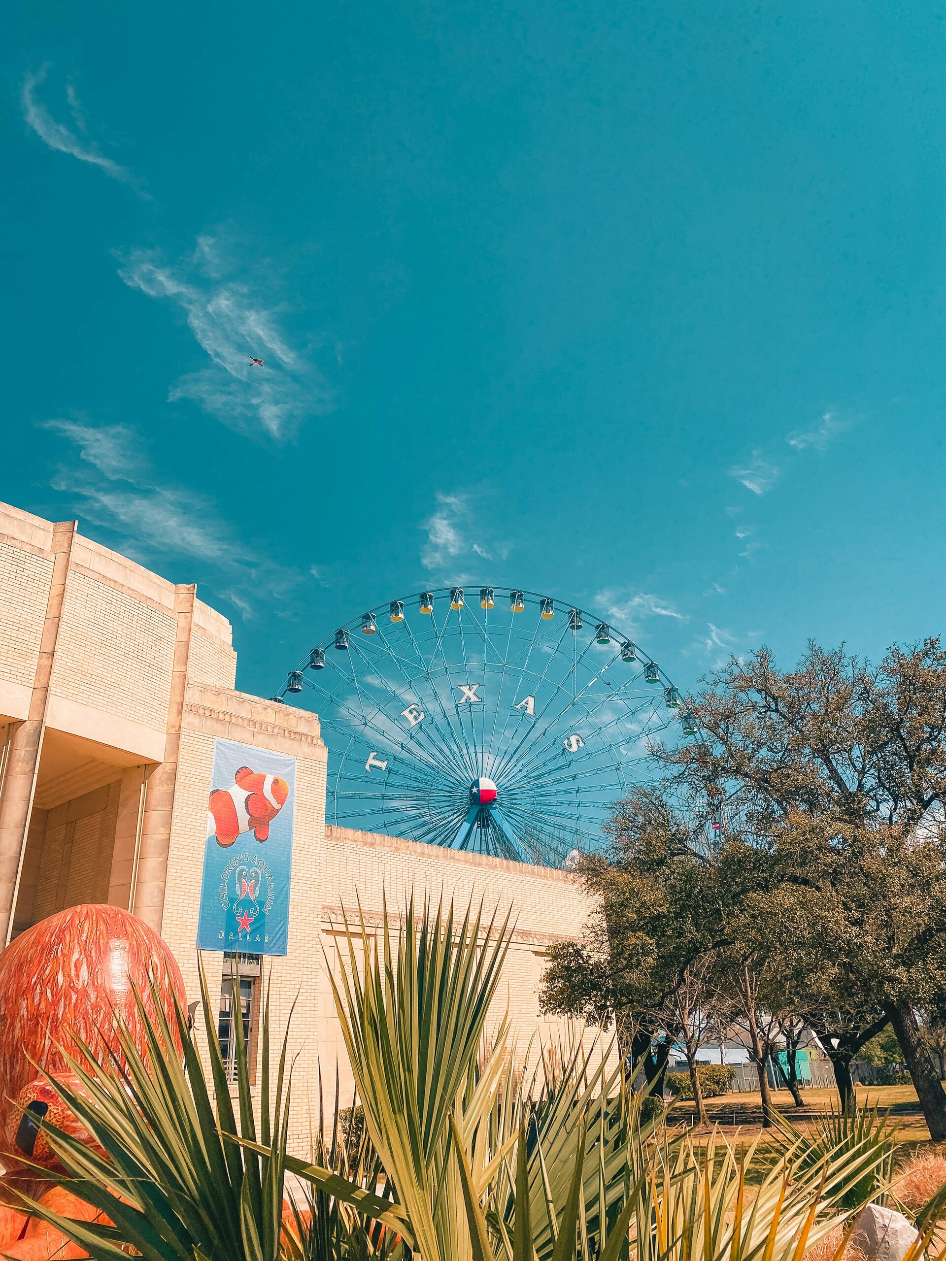 Large Ferris wheel rising behind a tall city building against a pastel sky
